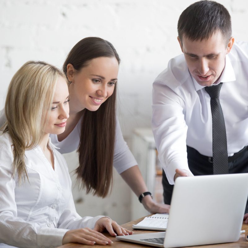 Business team working on project Teamwork concept. Group of three smiling young people working on project at office desk. Business team in formal wear using computer while discussing cooperative work